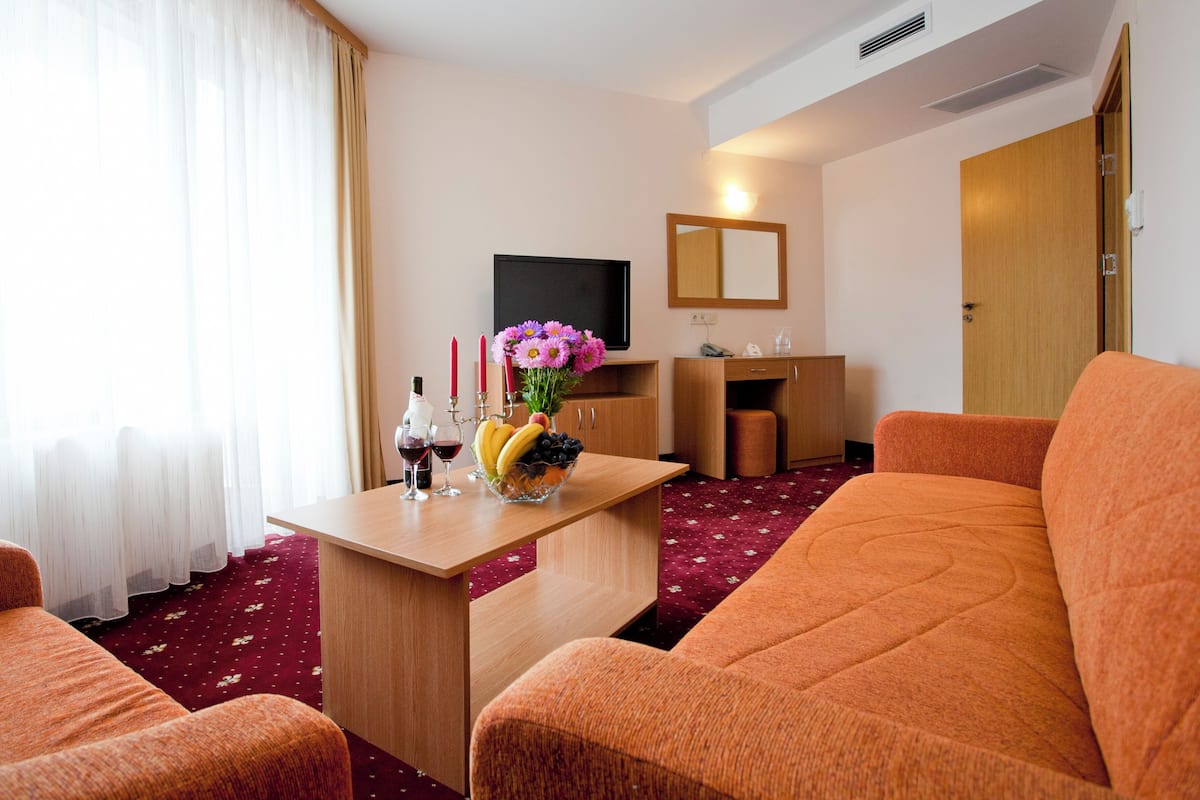 A hotel room with a sofa, a small table with a fruit bowl and candles, a TV, a mirror, and a wooden door.