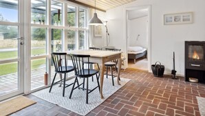 Ein gemütliches Zimmer mit Holztisch, Stühlen, Kamin und einem großen Fenster mit Blick auf Grünflächen.