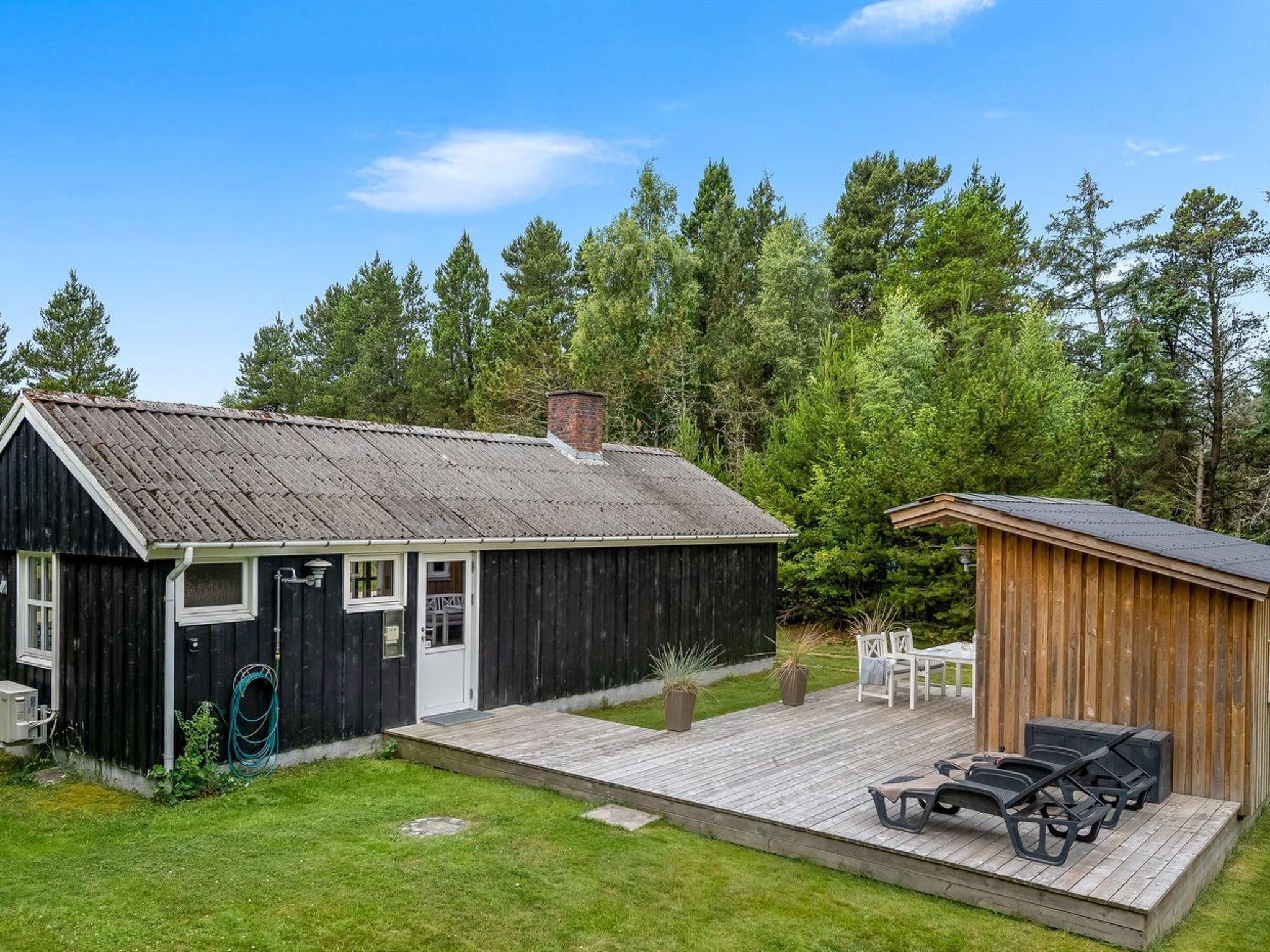 A rustic cabin with a wooden deck, a small porch, and a separate wooden structure with outdoor seating.