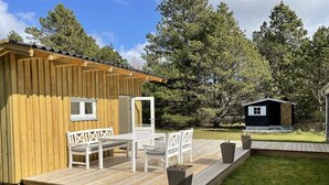 Eine Holzhütte mit einer Veranda, weißen Möbeln und einem kleinen Schuppen in einem bewaldeten Gebiet.