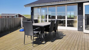 A deck with a table and chairs, a wooden fence, and a building with large windows. - "Ernbiorn" -  from the sea by Interhome (Harboøre)