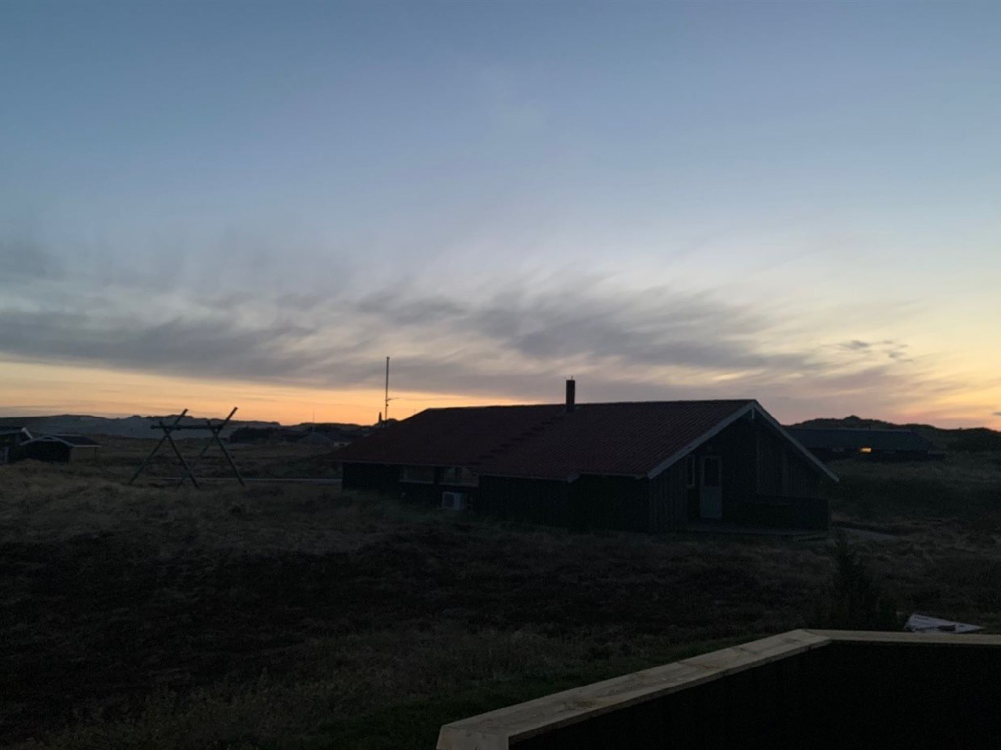 Una casa rural amb teulada vermella, envoltada d'àmples camps i un cel serè.