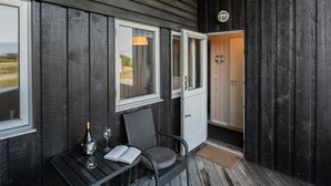 Eine Holzhütte mit überdachter Veranda, einem Tisch mit Flasche und Glas sowie einem Stuhl.