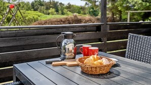 Ein Holztisch mit einer Metall-Kaffeekanne, roten Tassen, einem Korbkörbchen mit Brot und einem Holzschneidebrett.