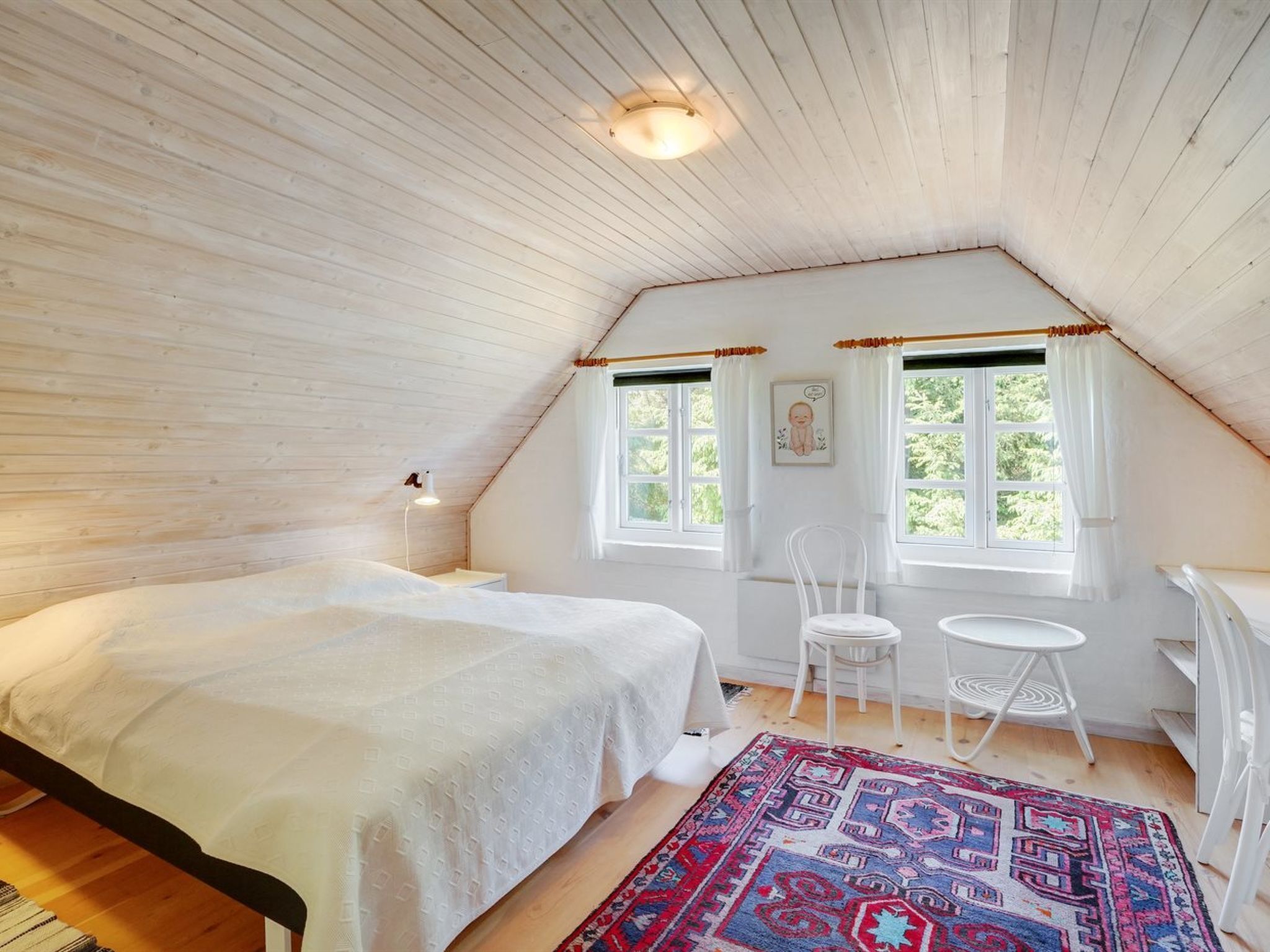 Un dormitorio con una cama grande, dos sillas, una mesita y un tapete colorido.