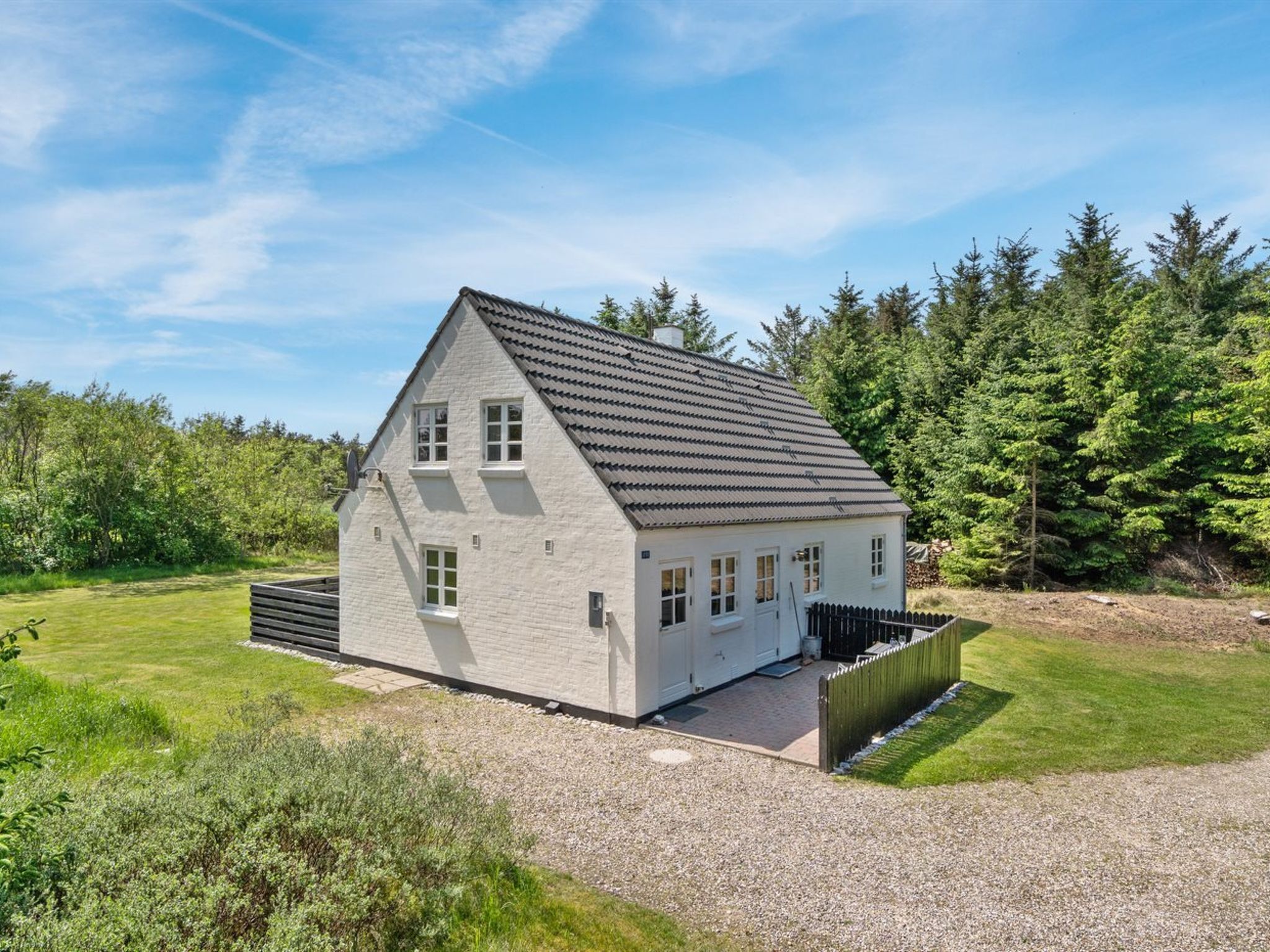 Een gelijkvloers huis met een schuin dak, een grindpad en een houten hek.