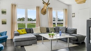 Un salon moderne avec un canapé d’angle, une table basse et une grande fenêtre agrémentée de rideaux.