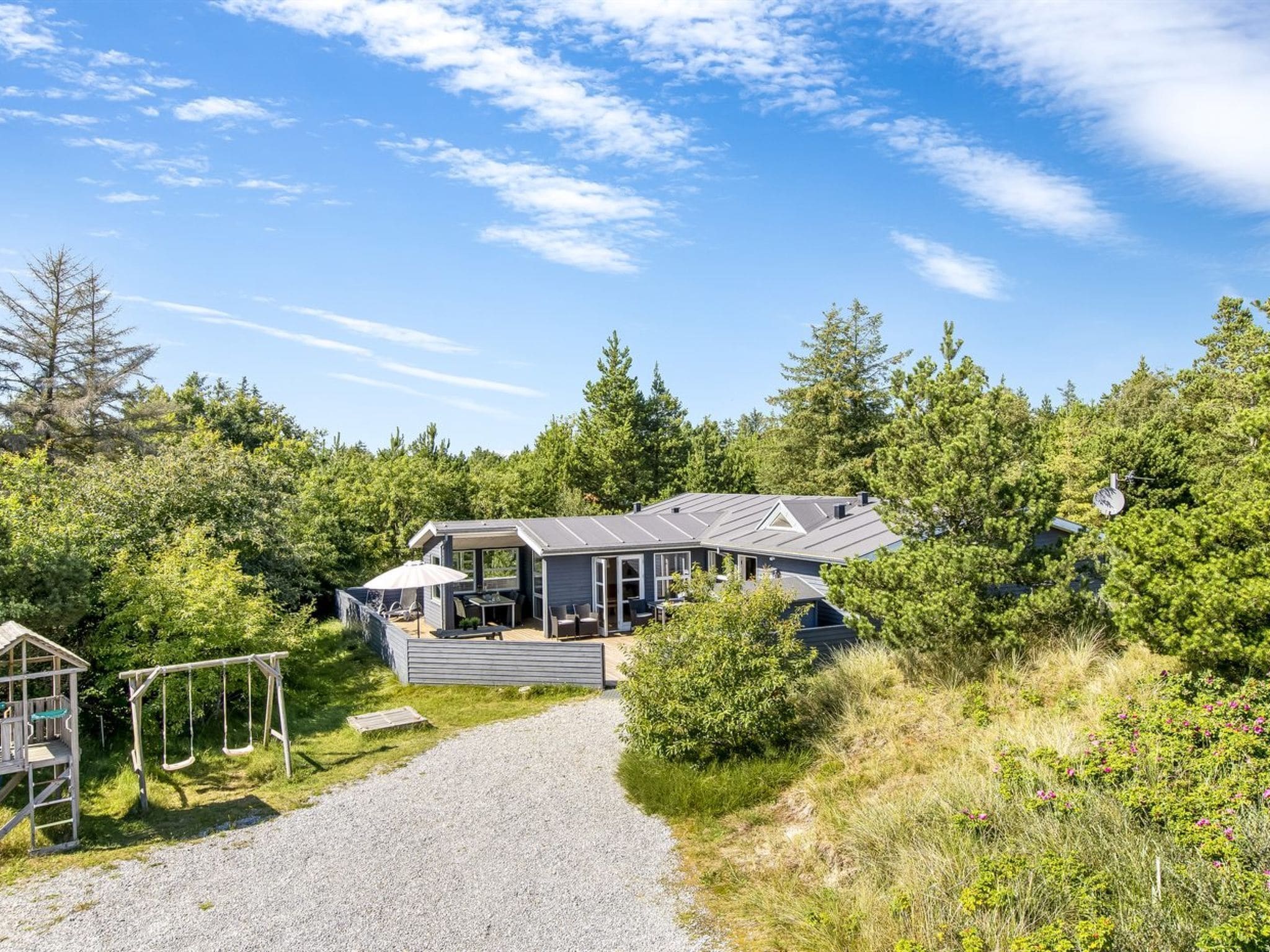 Et moderne hus med en overdækket terrasse, omgivet af tæt skov og en grussti.
