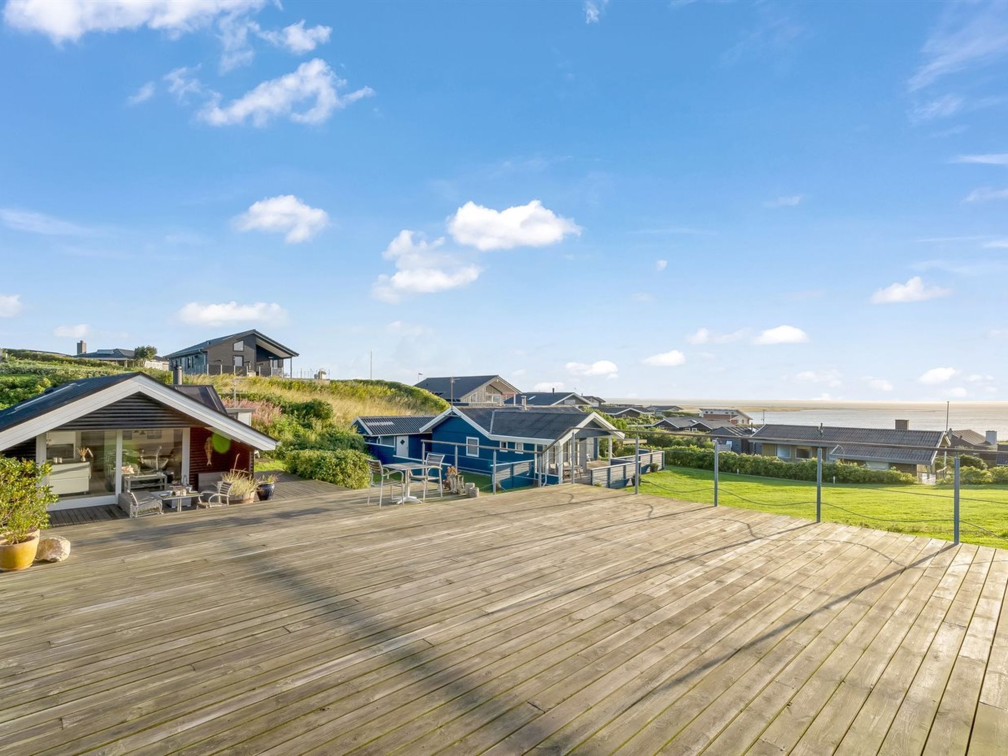 Een kustpand met een houten terras, meerdere huizen en uitzicht op zee.