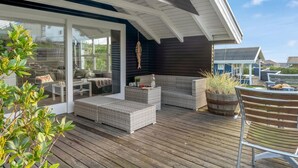 A covered outdoor seating area with wicker furniture, a wooden deck, and a view of neighboring houses.
