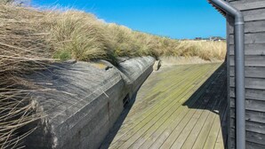 A wooden boardwalk adjacent to a concrete barrier with grass and sand dunes in the background. - "Adelita" - 100m from the sea by Interhome (Løkken)
