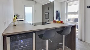 Eine moderne Küche mit Kochinsel, Barhocker, Geschirrspüler und Blick ins Freie.