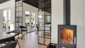Ein modernes Interieur mit Kaminofen, Glastüren zu einem Außenbereich und einem Esstisch mit Stühlen.