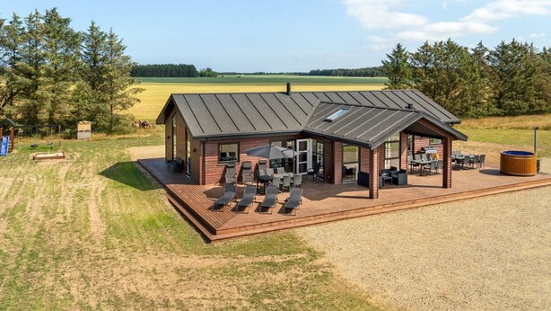 Eine Holzhütte mit einer Terrasse, Sitzgelegenheiten im Freien und Blick auf ein Feld.