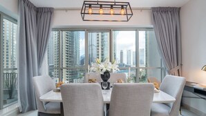 Un comedor con una mesa dispuesta para cuatro personas, ventanas grandes con cortinas y vistas a la ciudad.