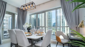 Comedor con una mesa lista para cuatro, ventanas grandes con cortinas y vista a edificios altos.