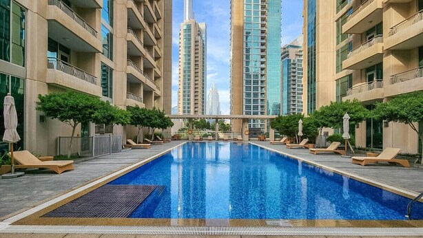 Una piscina con sillones reclinables y sombrillas, rodeada de edificios altos.
