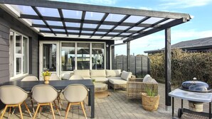 An outdoor patio with a covered seating area, a dining table with chairs, and a grill.