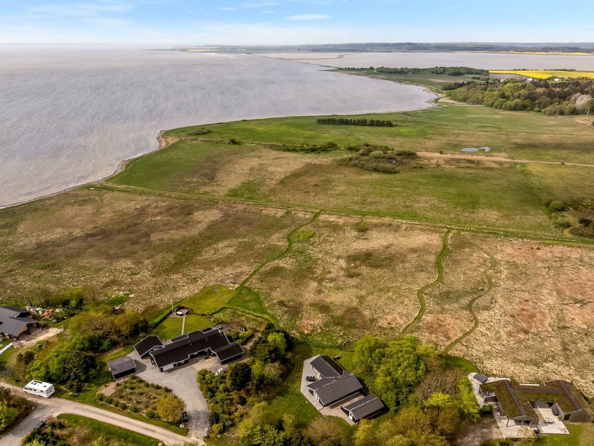 Vue aérienne d’une propriété située sur la côte, avec une grande maison, un bâtiment plus petit et un véhicule garé.