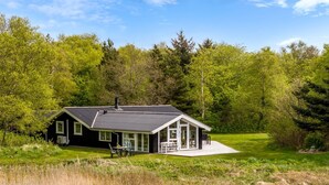 A two-story house with a covered porch, surrounded by a grassy field and dense trees. - "Eske" - 200m to the fjord by Interhome (Aabybro)