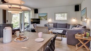 A modern living room with a sofa, coffee table, and dining area with a kettle and plates. - "Tjordis" - 600m to the fjord by Interhome (Hvide Sande)