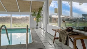 Un espace piscine intérieure moderne, avec une vue dégagée sur l’extérieur, un plafond en bois et une plante en pot.