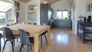 A modern kitchen with a central island, a dining area with a wooden table and chairs, and a large window providing natural light. - "Mayke" - 900m from the sea by Interhome (Løkken)