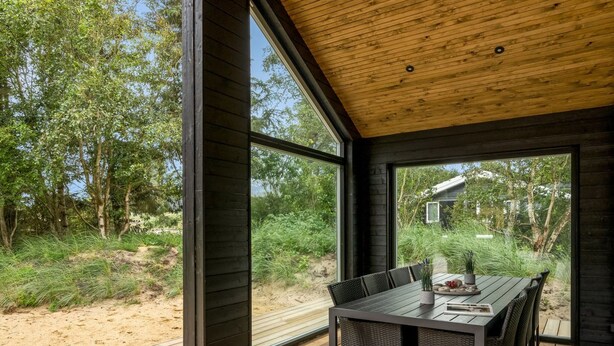 Een modern terras met een houten dek, een tafel met stoelen en uitzicht op het omliggende groen.