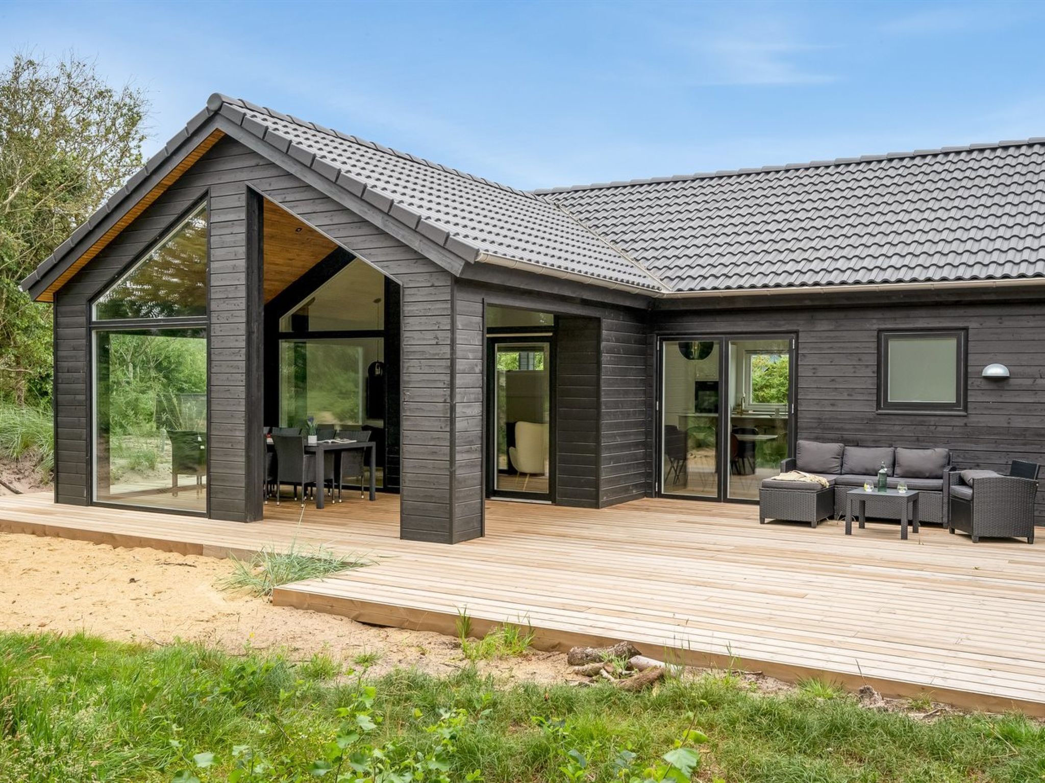 A modern house with a large deck, a dining area, and a seating area with outdoor furniture.