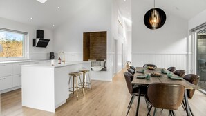 Een moderne keuken met een centraal eiland, barkrukken en een eethoek met een houten tafel en stoelen.