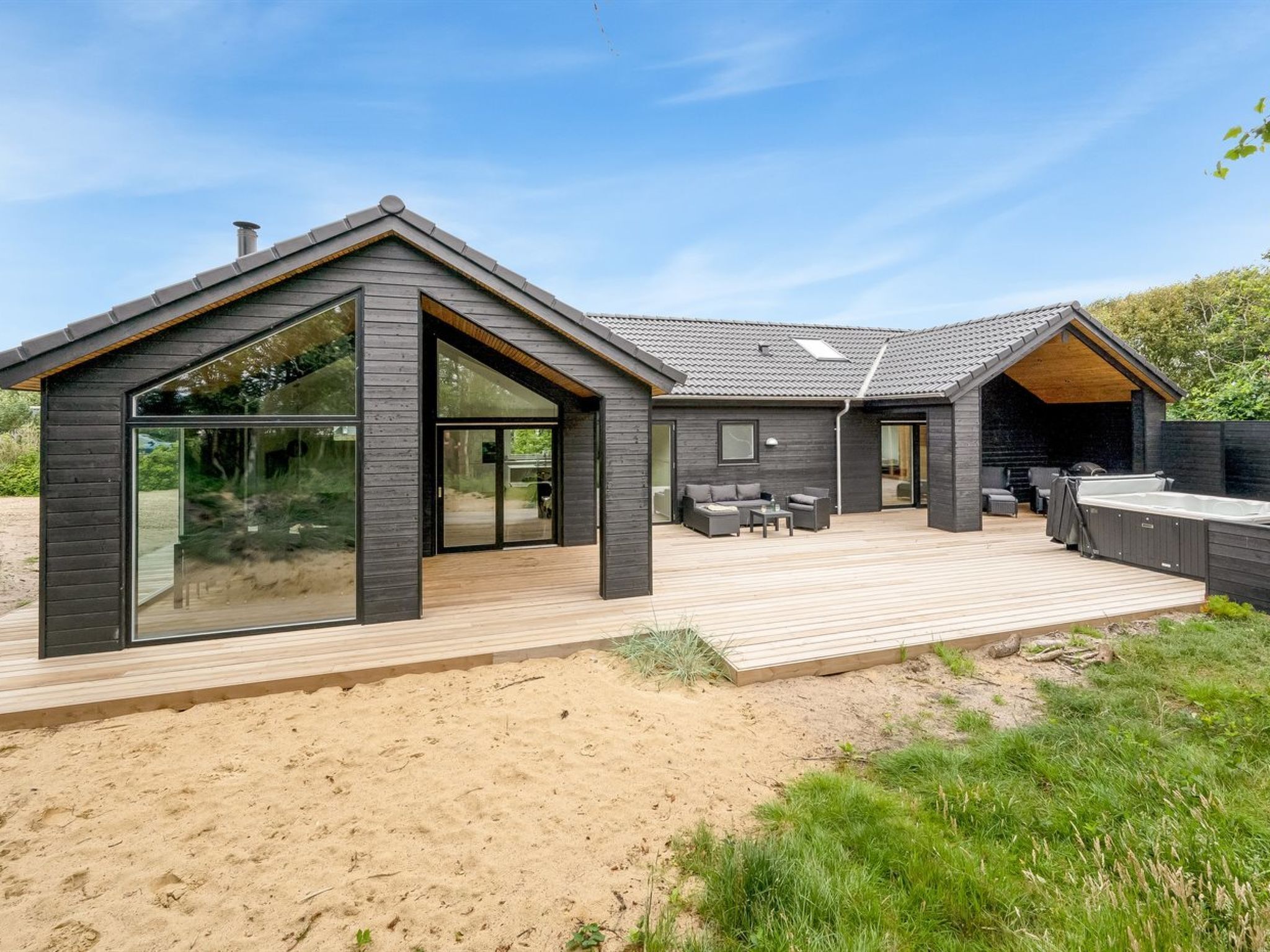 A modern house with a wooden deck, large glass windows, and a covered outdoor seating area.