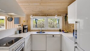 Een moderne keuken met witte kastjes, een inbouwfornuis, een vaatwasser en een raam met uitzicht op groen.
