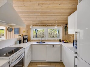 A modern kitchen with white cabinetry, a built-in stove, a dishwasher, and a window with a view of greenery. - "Ømod" - 300m from the sea by Interhome (Løkken)
