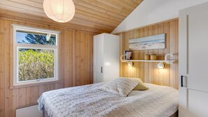 Een slaapkamer met een bed, een raam, houten wanden, een plank met boeken en een hanglamp.