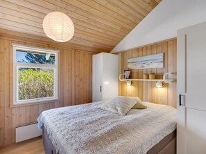A bedroom with a bed, a window, wooden walls, a shelf with books, and a hanging light fixture. - "Ømod" - 300m from the sea by Interhome (Løkken)