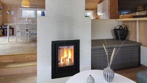 Een moderne woonkamer met een open haard, houten plafond en een eetgedeelte met witte stoelen.