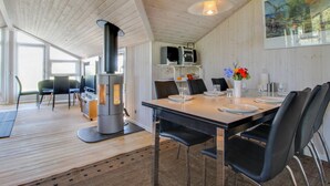A dining area with a wooden table set for two, black chairs, a wood-burning stove, and a painting on the wall.