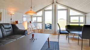 A modern interior with a black leather sofa, a dining table, and chairs. Large windows provide natural light and a view of the outdoors.