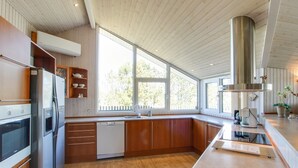 A modern kitchen with wooden cabinets, stainless steel appliances, and large windows offering a view of the outdoors.
