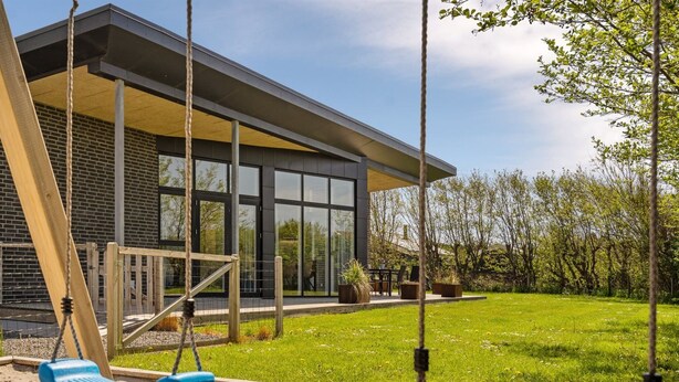Een modern huis met een groot raam, een schommel en een verzorgd gazon.