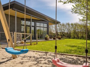 A modern house with a large glass window, a swing set, and a well-maintained lawn.
