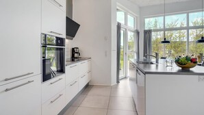 Een moderne keuken met witte kasten, een ingebouwde oven en een groot raam dat voor natuurlijk licht zorgt.