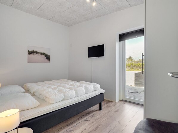 A bedroom with a bed, a TV, a painting, and a view of the outdoors.