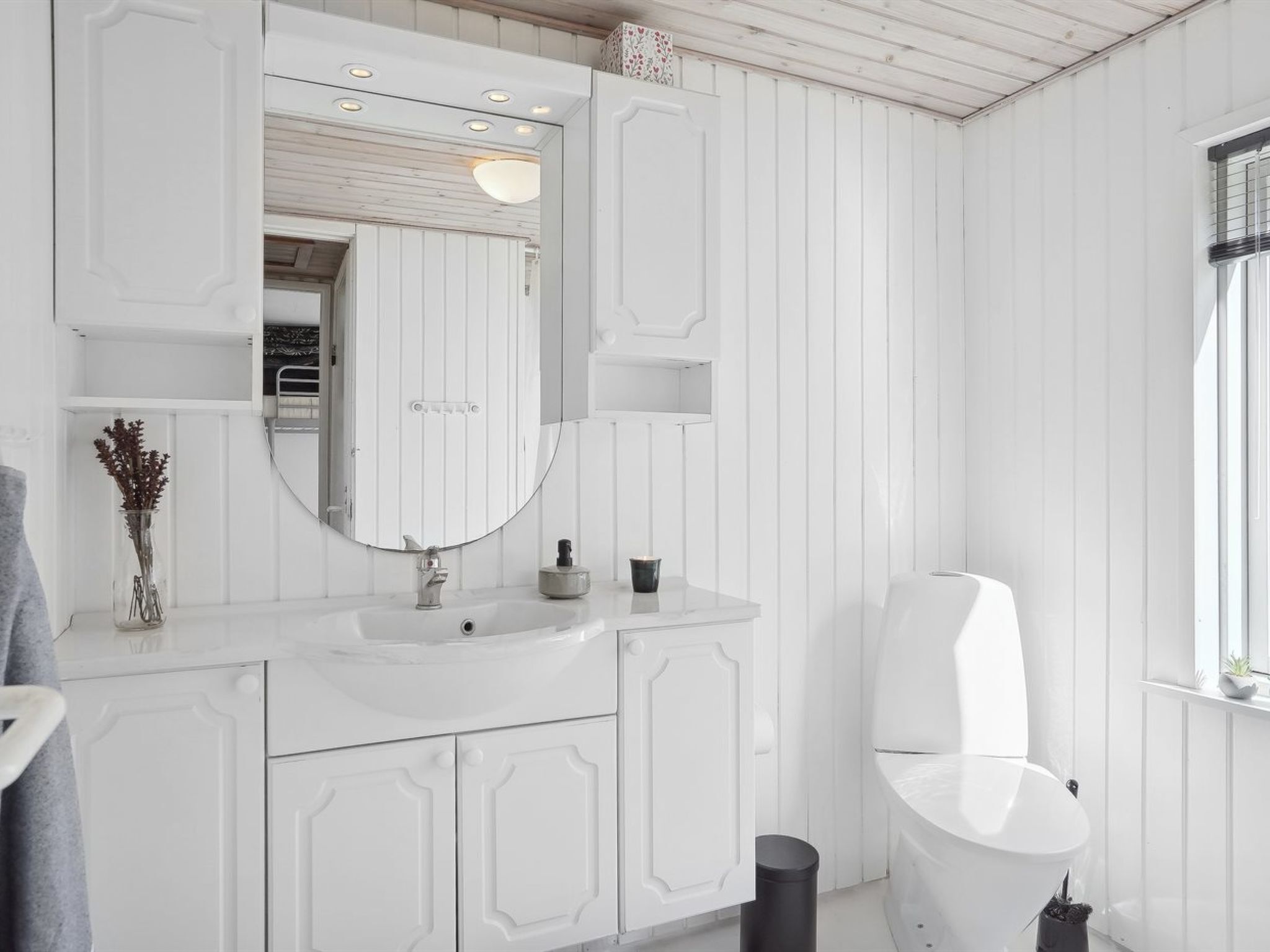 A modern bathroom with white cabinetry, a large mirror, a sink, and a toilet.