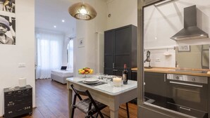 Una cocina moderna con horno empotrado, una zona de comedor con mesa de vidrio y un mueble negro con cajones.