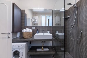 Casa de banho moderna com um espelho grande, uma pia, um chuveiro e uma máquina de lavar roupa.