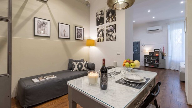 Una sala de estar con un sofá, una mesa con una vela, una botella de vino y cuadros en la pared.