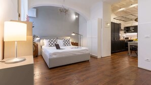 Un dormitorio con cama, mesita de noche, lámpara y vista a la cocina.
