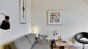 Un salon moderne avec un canapé gris, un fauteuil noir, une petite table avec des boissons et deux lampes fixées au mur.