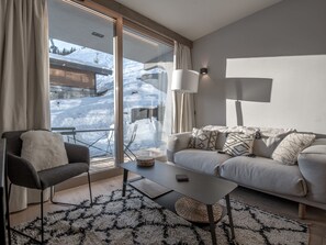 Un salon moderne comprenant un canapé, un fauteuil et une table basse, avec une vue sur un paysage enneigé grâce à de grandes fenêtres.
